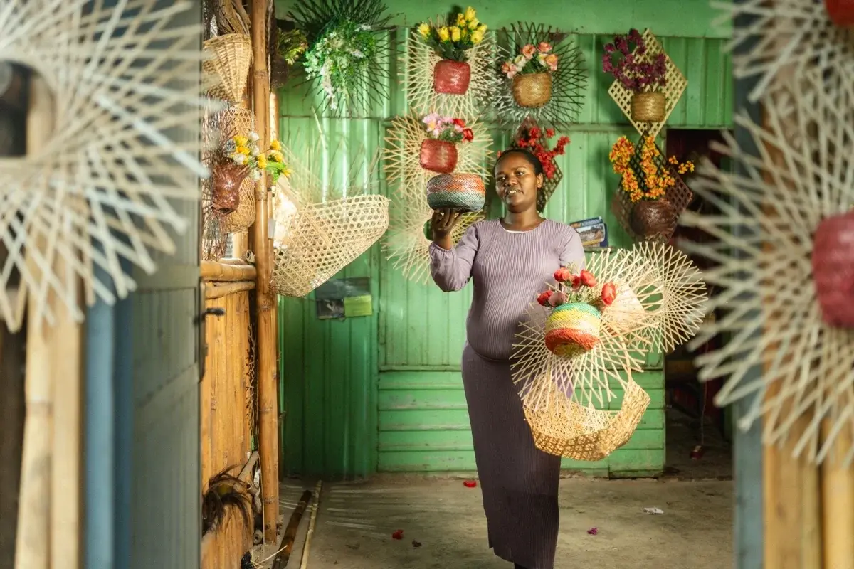 A young woman standing in her basket shop, displaying her woven bamboo baskets, SNV-RAYEE, Hulegeb Women's Bamboo Works, 2025.